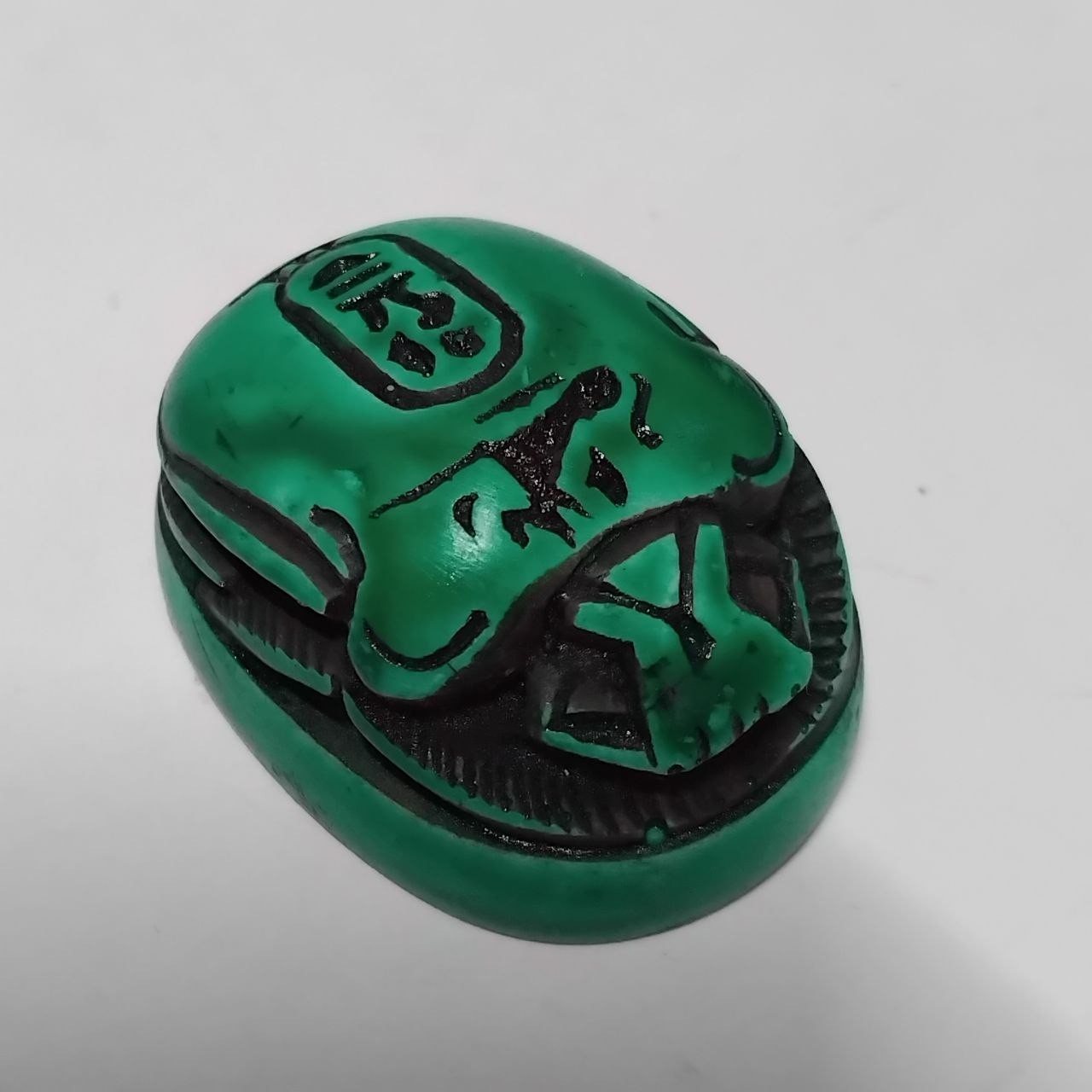 An Egyptian green stone scarab, inscribed with ancient hieroglyphic symbols.