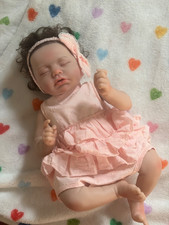 lifelike reborn baby doll wearing a pink ruffled dress and a matching picture